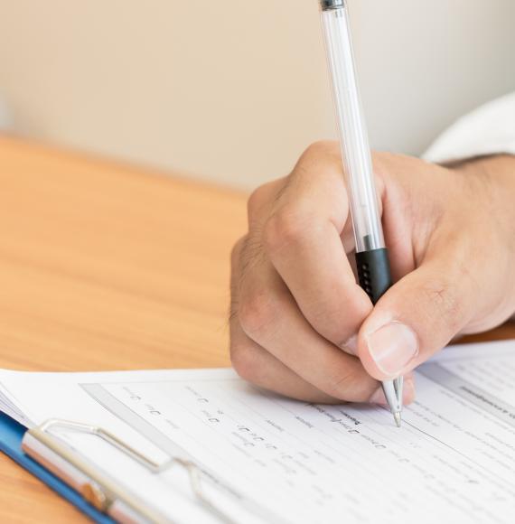 Close-up of a medical professional writing on a clipboard