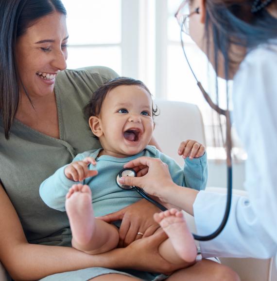 Shot of a baby sitting on her mother's lap while being examined by a doctor