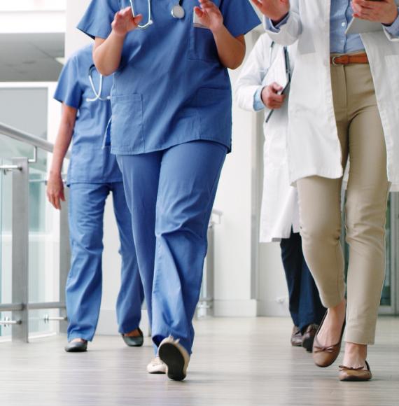 Image of the bottom half of healthcare workers walking down a corridor