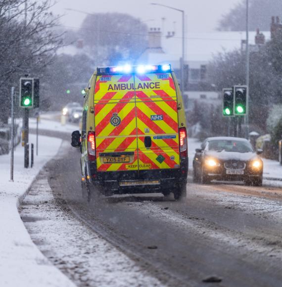 Rear-view shot of an NHS ambulance driving in the snow depicting the Scottish Government's health and social care plan for winter